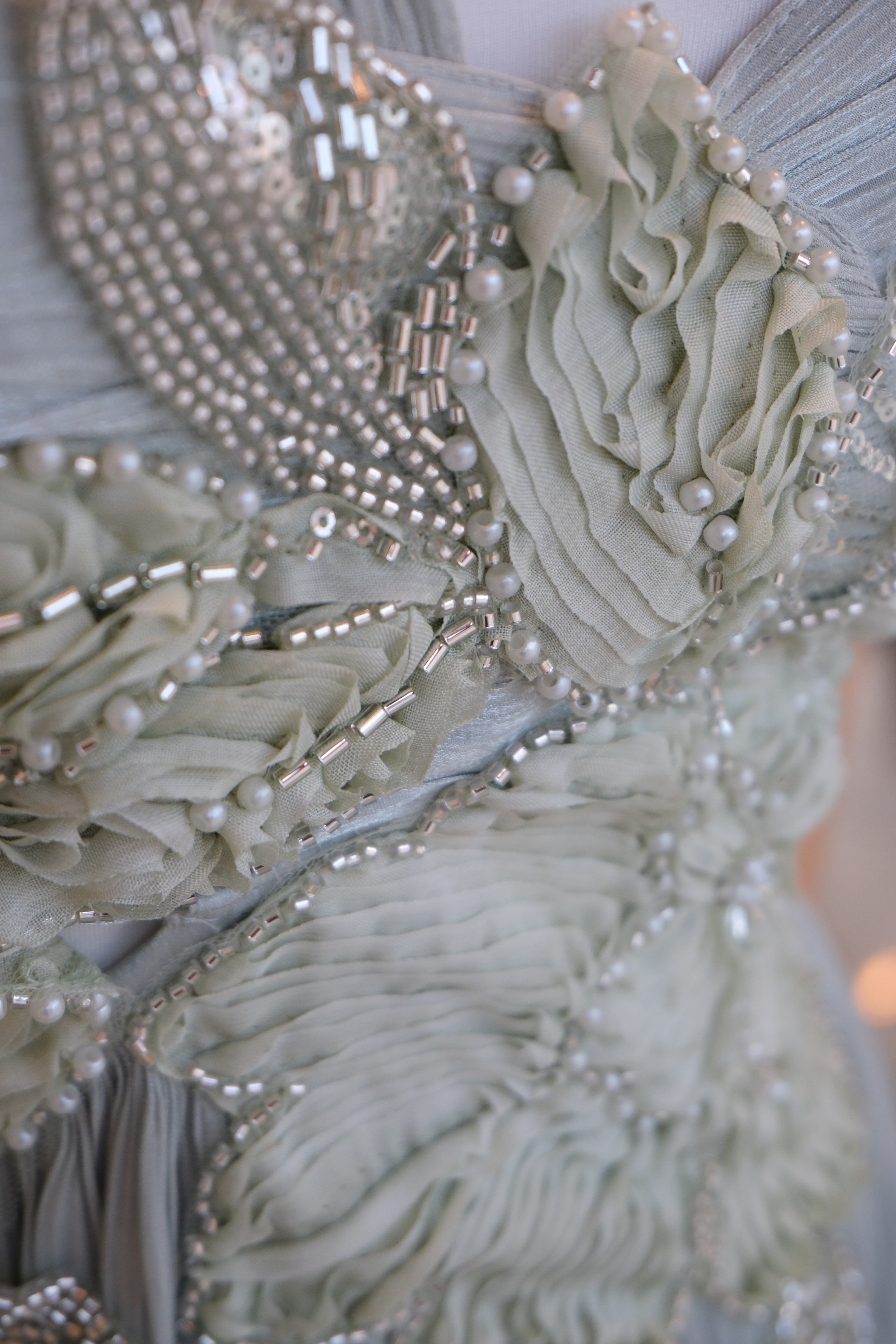 Close-up of hand-sewn silver beading and pearl embroidery on the pleated sage gown